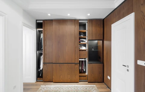 Dressing moderne avec armoires en bois naturel aux portes coulissantes ouvertes révélant rangements intérieurs, étagères et penderies