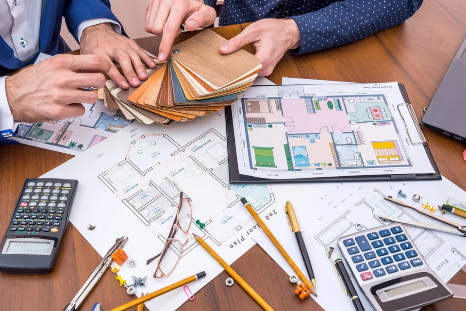 Réunion de travail autour d'une table en bois avec deux personnes consultant des nuanciers de matériaux et plans d'architecture