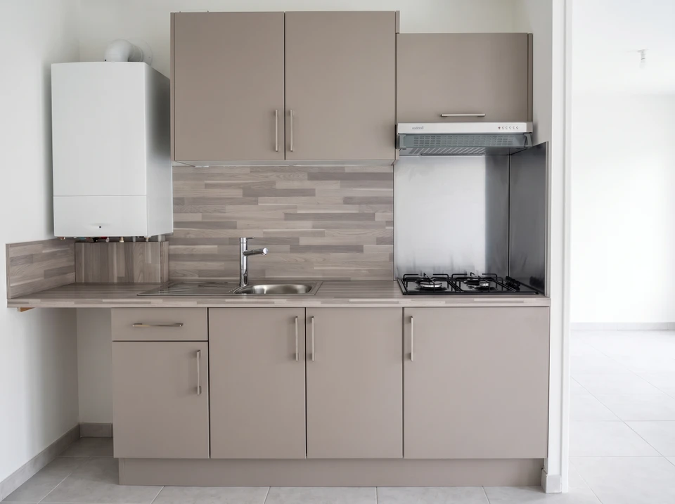Photographie d'une cuisine équipée en bois naturel installée dans un logement neuf de programme immobilier collectif ou logement social, avec mobilier sur mesure, finitions épurées et fonctionnelles, prise sous un angle montrant la qualité du travail de menuiserie et l'intégration harmonieuse du bois, sans présence de personnes.