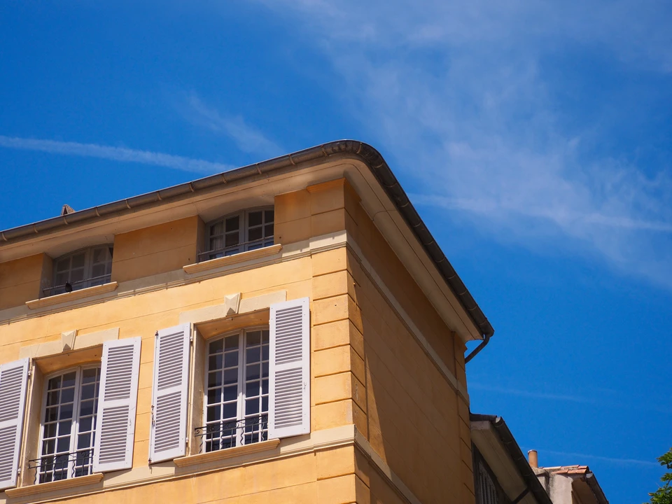 Photographie en situation réelle montrant des volets bois coulissants ou battants de qualité professionnelle, installés sur la façade d'un bâtiment, illustrant la finition, la précision d'exécution et l'aspect esthétique des volets bois sur mesure destinés à une clientèle professionnelle (immeuble collectif, bâtiment tertiaire ou collectivité).